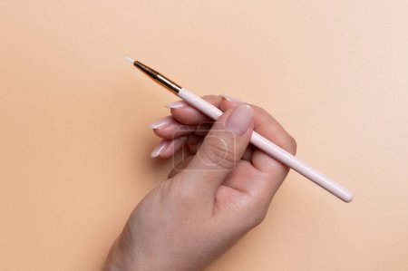 Small cosmetic brush  in woman hand close up view on beige color background