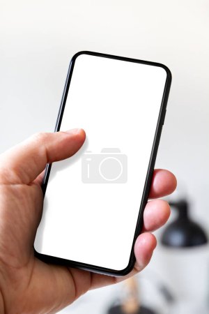 Téléchargez les photos : Main tenant un smartphone avec écran blanc vierge. fond de bureau blanc. - en image libre de droit