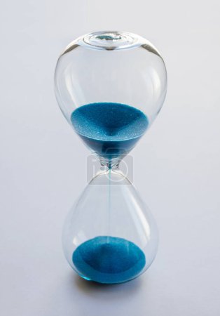 Photo for Hourglass containing blue sand isolated on white background. Concept of time passing - Royalty Free Image