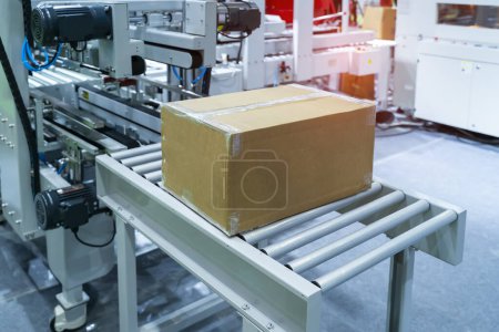 Téléchargez les photos : Boîte en carton de l'emballage du produit se déplace sur la bande transporteuse de la machine d'emballage automatique dans l'usine de fabrication - en image libre de droit