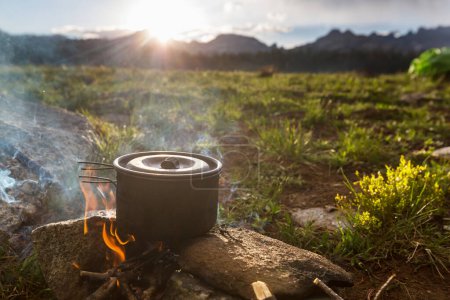 Téléchargez les photos : Bouilloire touristique sur le feu de feu de camp en camping dans la randonnée. Cuisiner la nourriture en forêt sur du bois de chauffage. - en image libre de droit