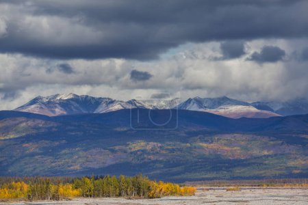 Foto de Picturesque Mountains of Alaska in autumn. Snow covered massifs, glaciers and rocky peaks, orange trees. Beautiful natural background. - Imagen libre de derechos