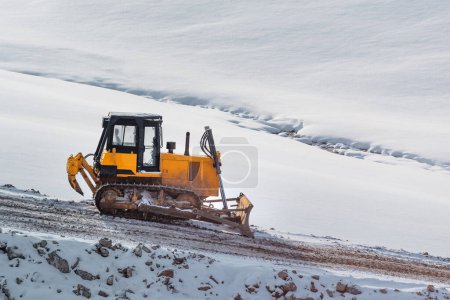 Téléchargez les photos : Machines de construction de routes lourdes bulldozer ou terrasseur sur chantier de construction sur une colline enneigée en hiver - en image libre de droit