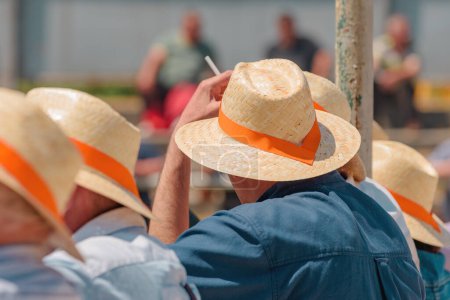 Photo for Group of unrecognizable casual people wearing straw hats with orange band at live equestrian public event on sunny summer day, selective focus - Royalty Free Image