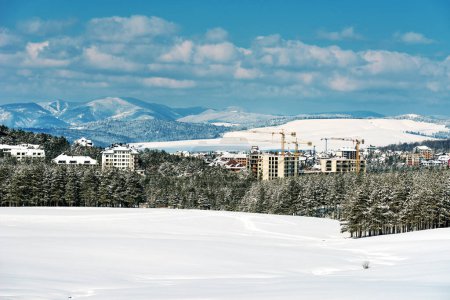Téléchargez les photos : Construction appartement et développement immobilier à Zlatibor en saison hivernale sous la neige, les bâtiments et les grues qui envahissent le paysage de la pinède - en image libre de droit