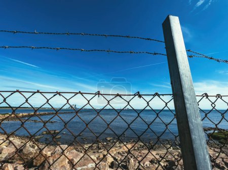 Foto de Valla de alambre de púas que rodea el área cerrada con el mar azul y el cielo sobre el horizonte como símbolos de libertad - Imagen libre de derechos
