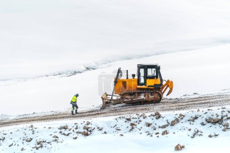 Téléchargez les photos : Ouvrier industriel devant bulldozer lourd sur le chantier de construction de routes en hiver - en image libre de droit
