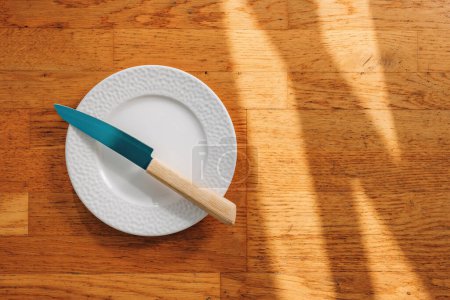 Photo for Kitchen knife and empty plate on wooden background, top view - Royalty Free Image