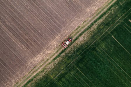 Photo for Aerial shot of agricultural tractor with crop seeder attached driving along dirt road through plowed fields, drone pov directly above - Royalty Free Image
