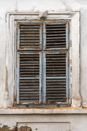Téléchargez les photos : Vieille fenêtre avec volets en bois usés sur le mur extérieur d'une vieille maison en ruine - en image libre de droit