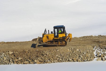 Téléchargez les photos : Travailleur méconnaissable conduisant un bulldozer industriel sur un chantier de construction de routes en hiver sur les collines de Zlatibor - en image libre de droit