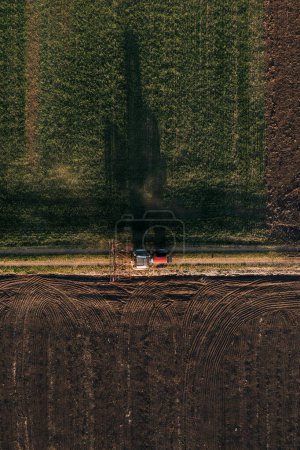 Foto de Vista aérea del tractor agrícola con timón conectado a la conducción en carretera de tierra después del trabajo en el campo - Imagen libre de derechos