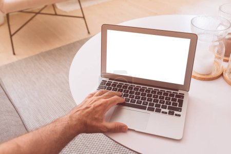 Photo for Man using laptop computer with blank mockup screen at living room coffee table, selective focus - Royalty Free Image
