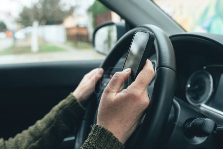 Téléchargez les photos : Closeup shot of female hand typing message on smartphone device, casual woman driver wearing green knitted sweater using mobile phone in vehicle interior, selective focus - en image libre de droit