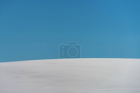 Téléchargez les photos : Abstract minimalistic winter landscape, snow covered hill with blue sky in background on sunny day, copy space included - en image libre de droit