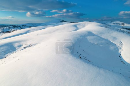 Foto de Foto aérea de la cima de la colina nevada iluminada por el sol poniente en el atardecer de invierno en Zlatibor, Serbia desde el punto de vista del dron. - Imagen libre de derechos