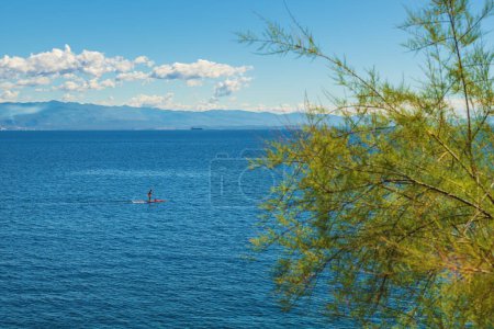 Téléchargez les photos : Unrecognizable person stand-up paddle boarding at Adriatic sea Kvarner gulf seen from the Lovran town coastline, selective focus - en image libre de droit