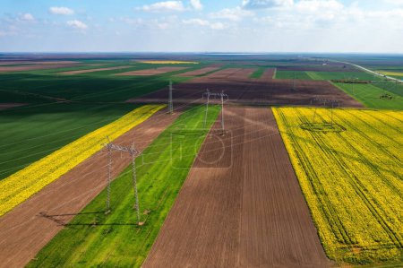 Téléchargez les photos : Aerial shot of transmission towers electricity pylons with power lines in cultivated agricultural field, drone pov high angle view - en image libre de droit