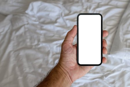 Foto de Male tourist in hotel bedroom holding smartphone with blank mockup screen for booking and reservation app or accommodation rating service - Imagen libre de derechos