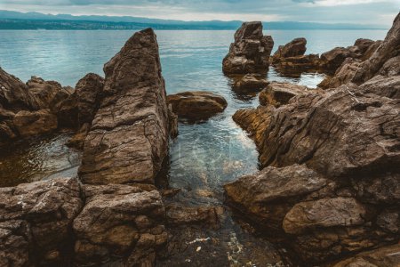 Foto de Kvarner gulf of Adriatic sea rocky coastline, large rocks at shoreline in old town of Lovran in Croatia. Selective focus. - Imagen libre de derechos