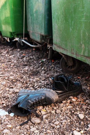 Téléchargez les photos : Chaussures noires usées par des poubelles dans la rue, mise au point sélective - en image libre de droit
