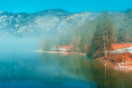 Foto de Lago Bohinj paisaje en la mañana de invierno, niebla que sube sobre el agua glacial limpia en el parque nacional esloveno Triglav y famoso destino de viaje - Imagen libre de derechos
