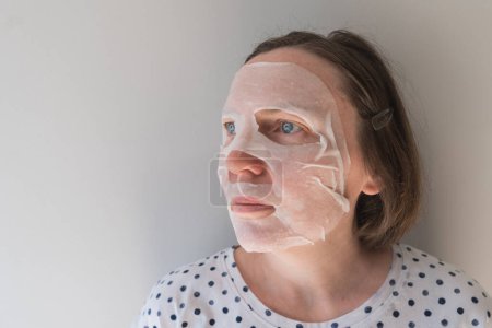 Photo for Adult caucasian female using anti-aging hydrating sheet face mask with hyaluron, selective focus - Royalty Free Image