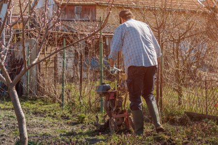 Téléchargez les photos : Agriculteur effectuant le travail du sol de jardin avec une vieille machine agricole de labourage pauvre, foyer sélectif - en image libre de droit