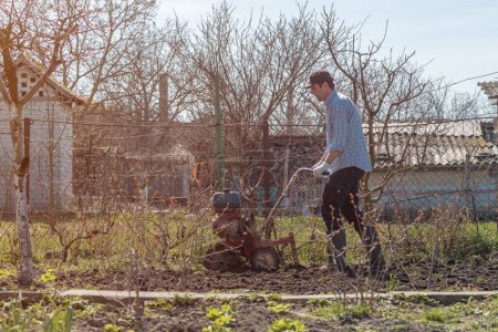 Foto de Agricultor que realiza labranza del suelo del jardín con la vieja máquina agrícola pobre del cultivador del cultivador, foco selectivo - Imagen libre de derechos