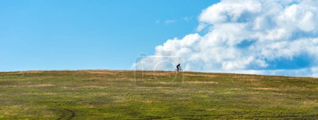 Téléchargez les photos : Silhouette de cycliste méconnaissable profitant du vélo hors route et du vélo de montagne activité sportive de plein air sur les collines de Zlatibor avec ciel bleu et nuages en arrière-plan - en image libre de droit