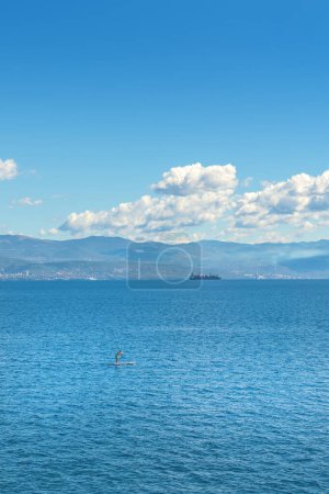Foto de Persona irreconocible stand-up paddle boarding en el mar Adriático Golfo de Kvarner visto desde la costa de la ciudad de Lovran, enfoque selectivo - Imagen libre de derechos