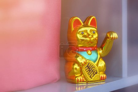 Photo for Maneki neko, japanese waving cat adorning the storefront of a trendy clothes boutique. This lucky feline figurine is popular symbol of good fortune and prosperity in Asian culture. Selective focus. - Royalty Free Image