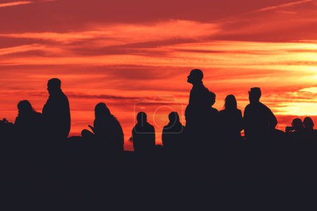 Foto de Back lit group of people in silhouette enjoying amazing summer sunset with orange sky in background - Imagen libre de derechos