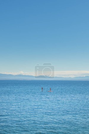Foto de Personas irreconocibles se levantan remando en el mar Adriático Golfo de Kvarner visto desde la costa de la ciudad de Lovran, enfoque selectivo - Imagen libre de derechos