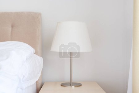 Téléchargez les photos : Lampe de chevet élégante avec abat-jour blanc sur la table de nuit dans la chambre, mise au point sélective - en image libre de droit