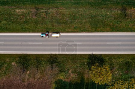 Téléchargez les photos : Vue aérienne du tracteur agricole tirant le réservoir fécal sur la route de campagne, point de vue du drone directement au-dessus - en image libre de droit