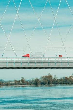 Photo for Red semi-truck crossing the bridge over Danube river in Novi Sad on sunny spring day - Royalty Free Image