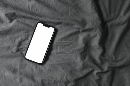Photo for Smart mobile phone with blank mockup screen on wrinkled bed linen, top view - Royalty Free Image