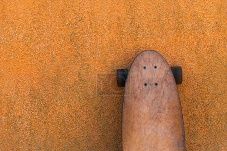 Foto de Longboard de skate usado apoyado en la sucia pared naranja, enfoque selectivo - Imagen libre de derechos