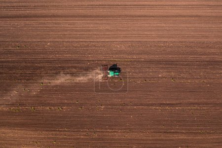 Photo for Agricultural tractor with tiller attached performing field tillage before the sowing season, aerial shot seen from the drone pov top down - Royalty Free Image
