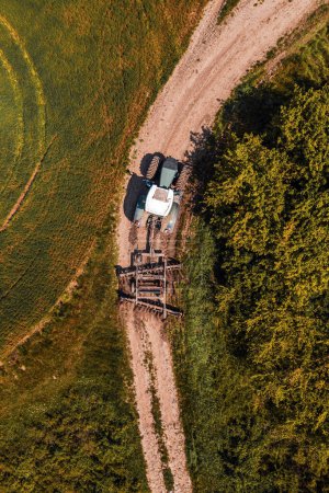Photo for Aerial view of agricultural tractor with tiller attached on dirt road driving to the field, drone pov top view - Royalty Free Image