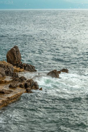 Foto de Ondas oceánicas frenando en las rocas de la costa cubriéndolas de espuma blanca en el soleado día de verano - Imagen libre de derechos