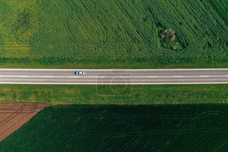 Photo for Driving through cultivated landscape in spring. Aerial view of car on country road, drone pov. Transportation and commuting concept. - Royalty Free Image