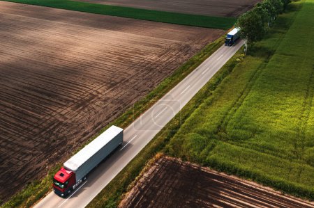Téléchargez les photos : Deux grands semi-camions sur route de campagne vu du point de vue du drone, prise de vue aérienne du concept de camionnage et de logistique, vue grand angle - en image libre de droit