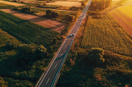 Photo for Aerial shot of traffic on countryside road in summer sunset, high angle view drone pov image of cars driving along the highway through Vojvodina in Serbia - Royalty Free Image