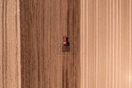 Photo for Red agricultural tractor with tiller attached performing field tillage before the sowing season, aerial shot seen from the drone pov top down - Royalty Free Image