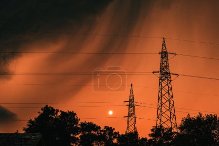 Photo for Dark ominous stormy clouds at orange summer sky, silhouettes of treetops and electricity pylon just before the rain, selective focus - Royalty Free Image