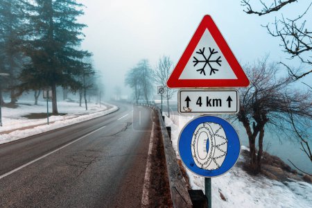 Photo for Beware of Ice or snow triangular warning sign and Chains required in winter traffic sign by the road, selective focus - Royalty Free Image