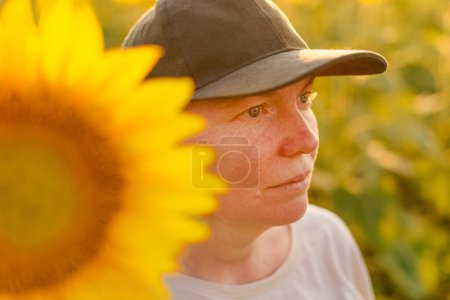 Photo for Female farm worker with trucker's hat in blooming sunflower field. Agriculture and farming concept. Selective focus. - Royalty Free Image