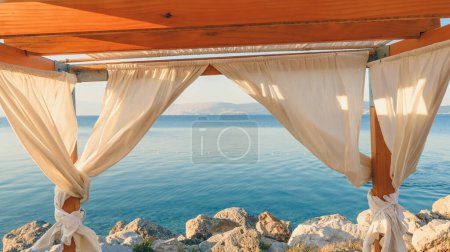 Téléchargez les photos : Pergola au bord de la mer avec rideaux en été matin, Voyage et vacances fond avec espace de copie - en image libre de droit